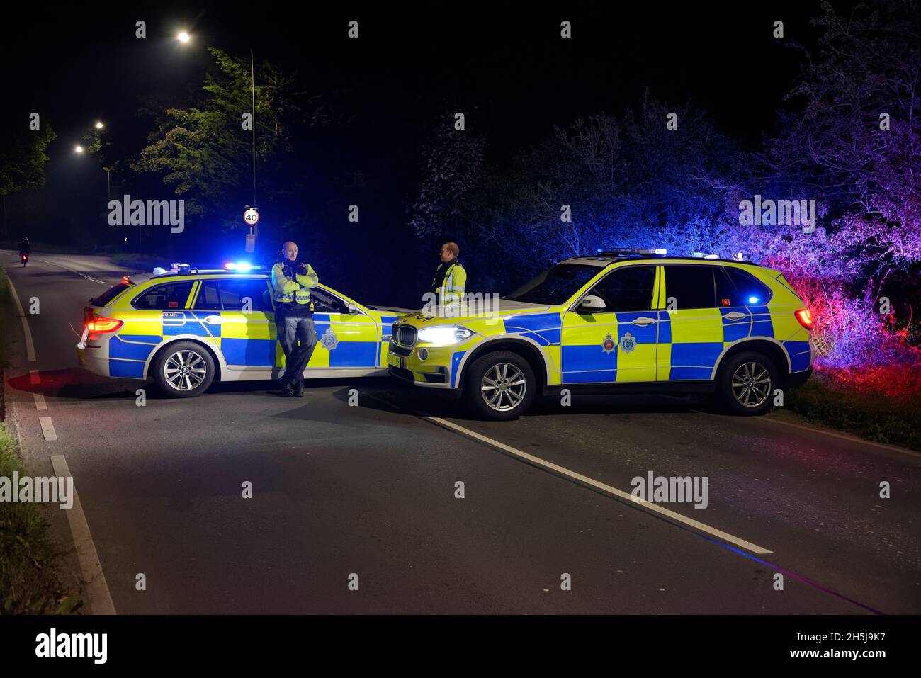 Due veicoli di polizia in Inghilterra nel 2021 che bloccano la strada. Due autisti della polizia in piedi. Foto Stock