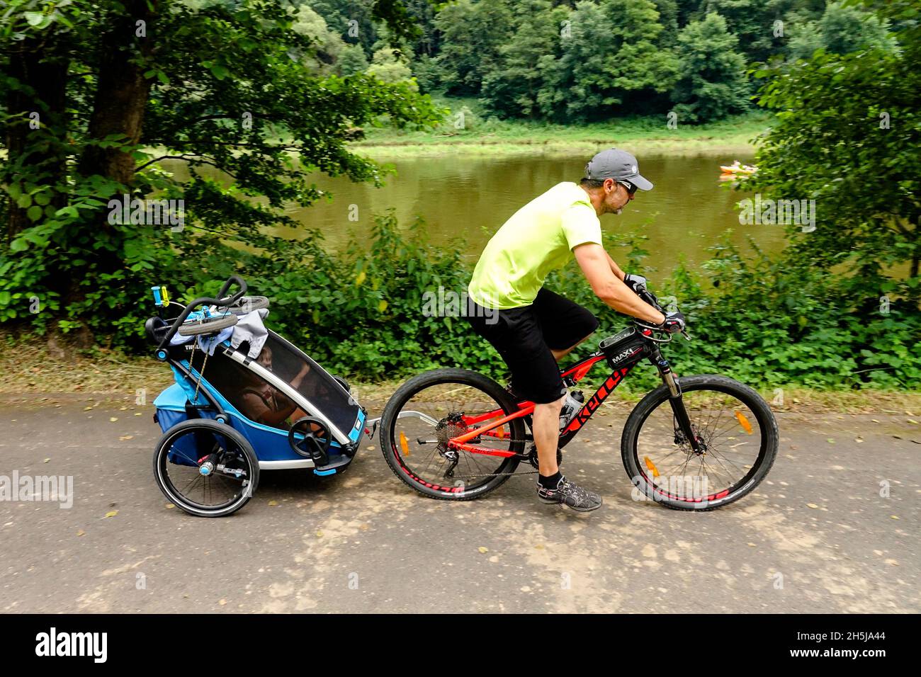Uomo in bicicletta lungo il percorso ciclabile con rimorchio per bici bambino all'interno Foto Stock