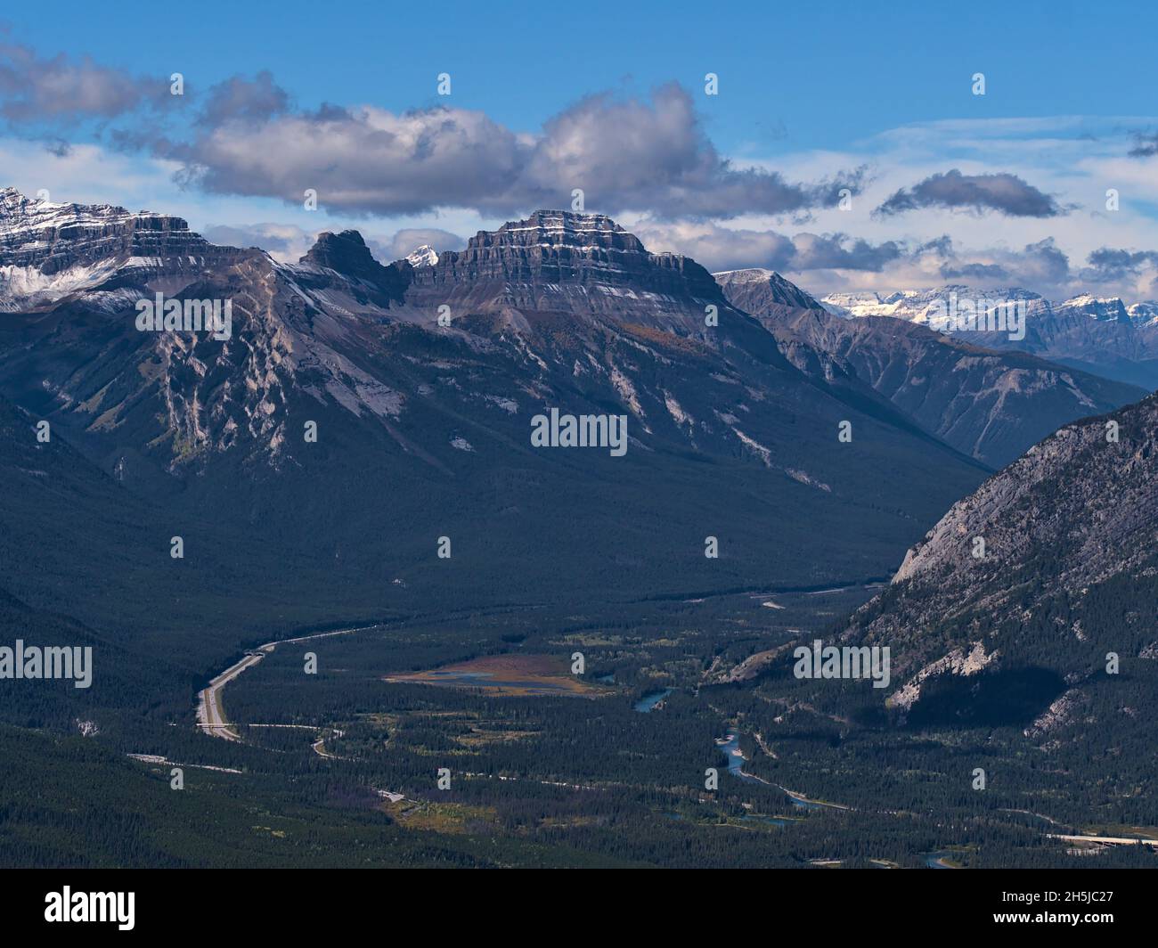 Vista ad alto angolo delle Montagne Rocciose (Massive Range) con cime innevate sopra la Bow Valley con foreste, torrente tortuoso e Trans-Canada Highway. Foto Stock