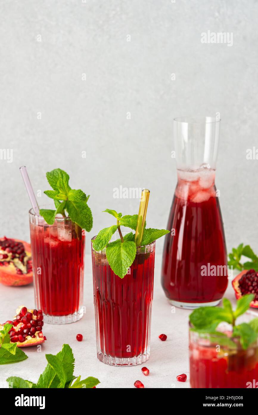 Rinfrescante succo di melograno in bicchieri con paglia di menta e vetro, caraffa di succo di frutta e ghiaccio, bevanda fredda Foto Stock