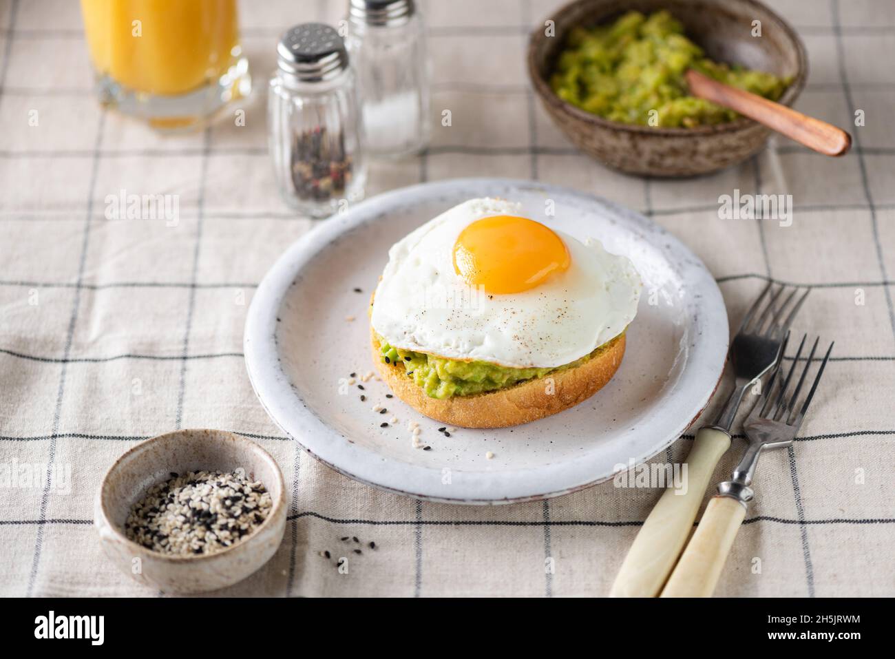 Prima colazione avocado toast con uova fritte su un piatto, biancheria sul tavolo Foto Stock