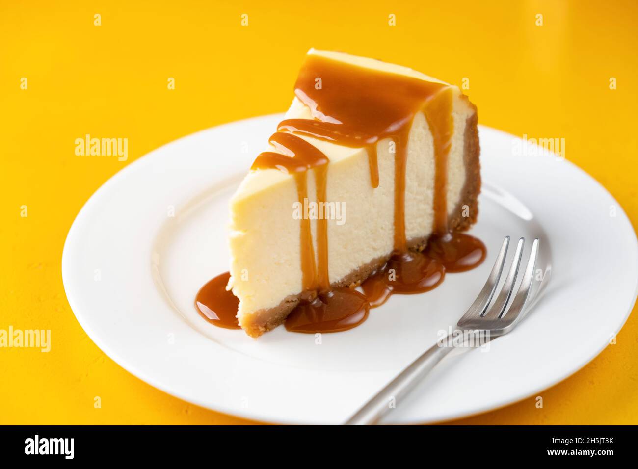 Fetta di cheesecake con salsa al caramello salato sul piatto, isolata su sfondo giallo Foto Stock