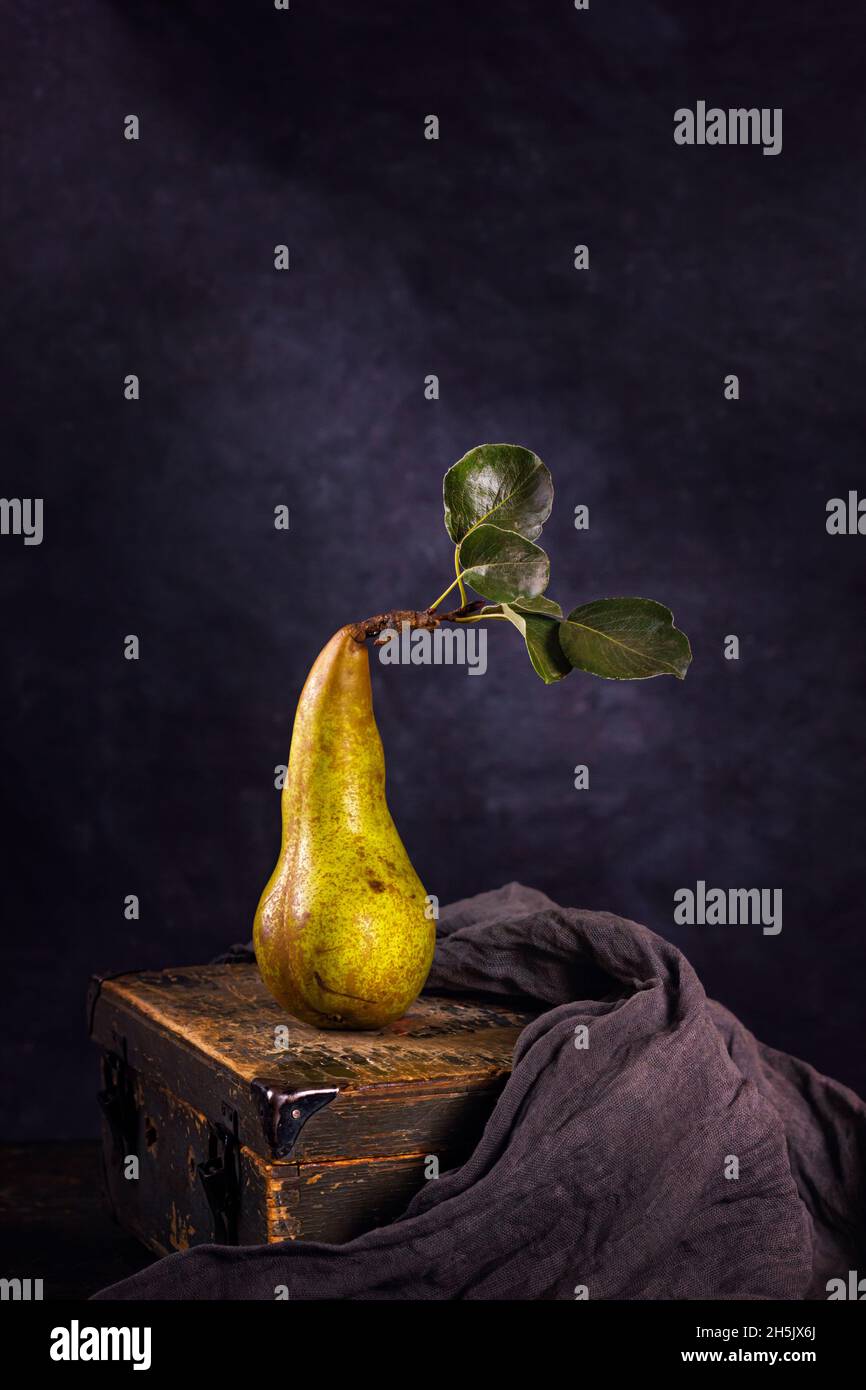Vita rurale morta, fotografia oscura a basso tasto - vista di una pera di conferenza solitaria su una vecchia scatola di legno, primo piano con fuoco selettivo Foto Stock