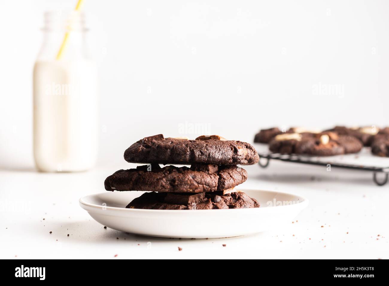 accatastate biscotti al cioccolato fondente con una bottiglia di latte sullo sfondo e un vassoio di biscotti Foto Stock