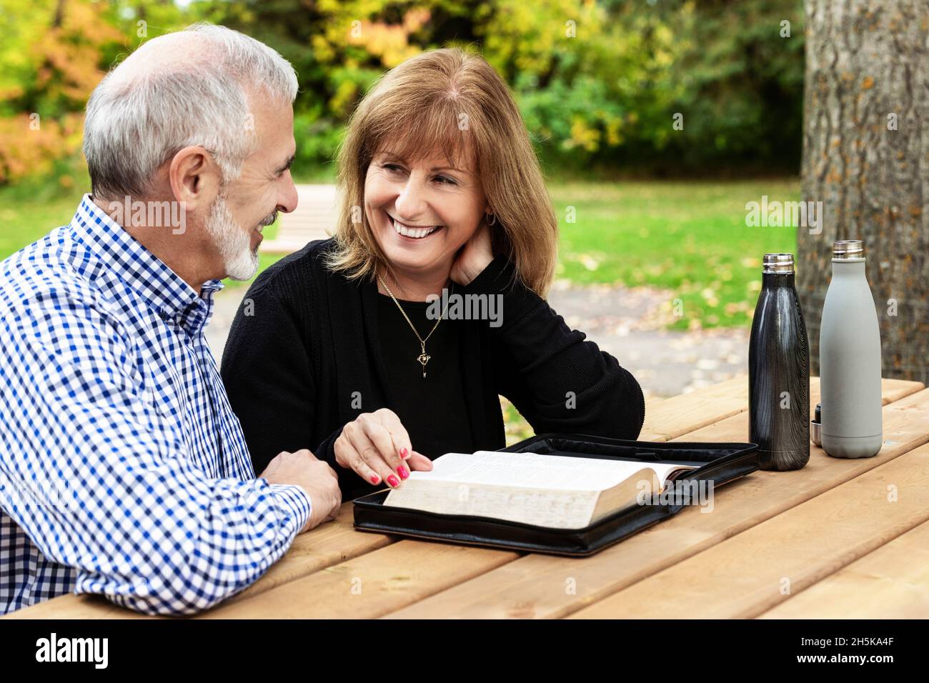 Una coppia matura che condivide insieme il tempo devozionale e studia la bibbia a un tavolo da picnic in una calda giornata di autunno in un parco cittadino Foto Stock