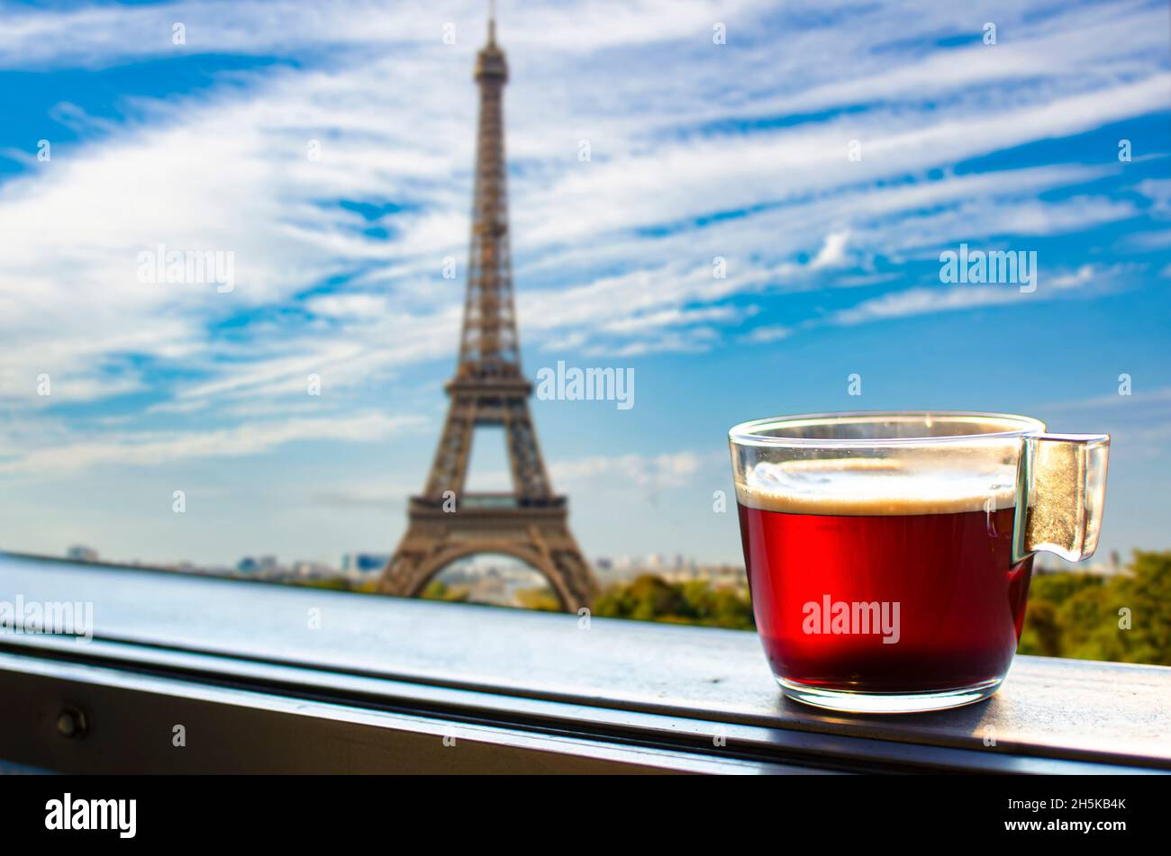Tazza di vetro di caffè o tè sul balcone con vista sulla Torre Eiffel e sullo sfondo dello skyline di Parigi. Vista soleggiata di un bicchiere di tè con vista sulla Torre Eiffel Foto Stock