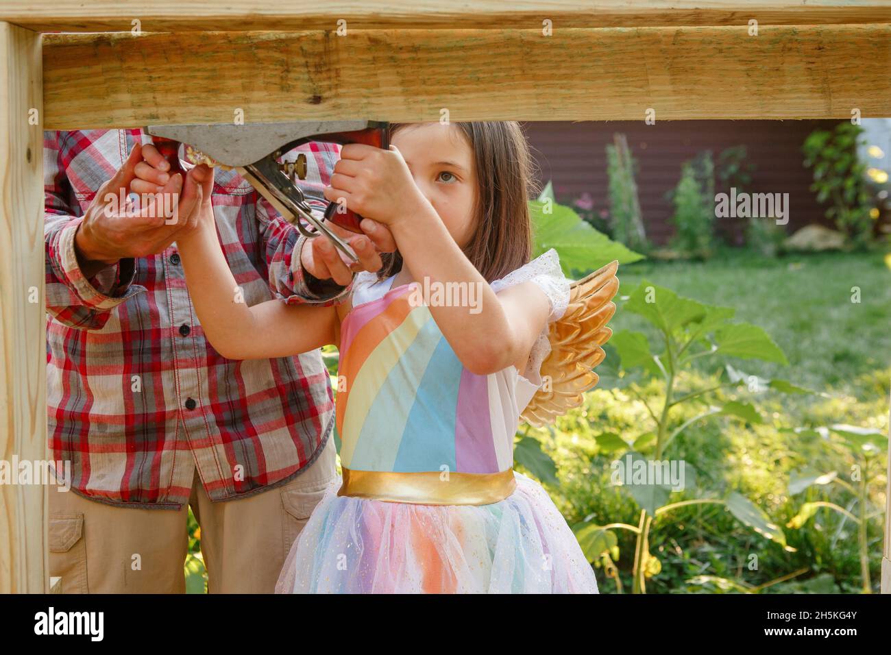 La bambina in costume usa uno strumento aereo a mano con l'aiuto del padre Foto Stock