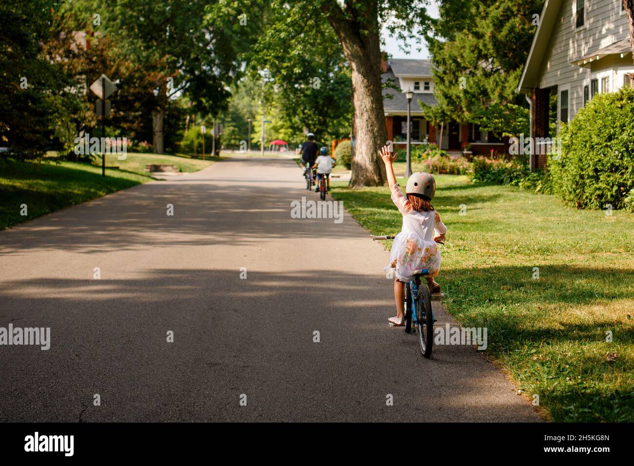 Un bambino piccolo in bicicletta con la famiglia solleva una mano in su Foto Stock