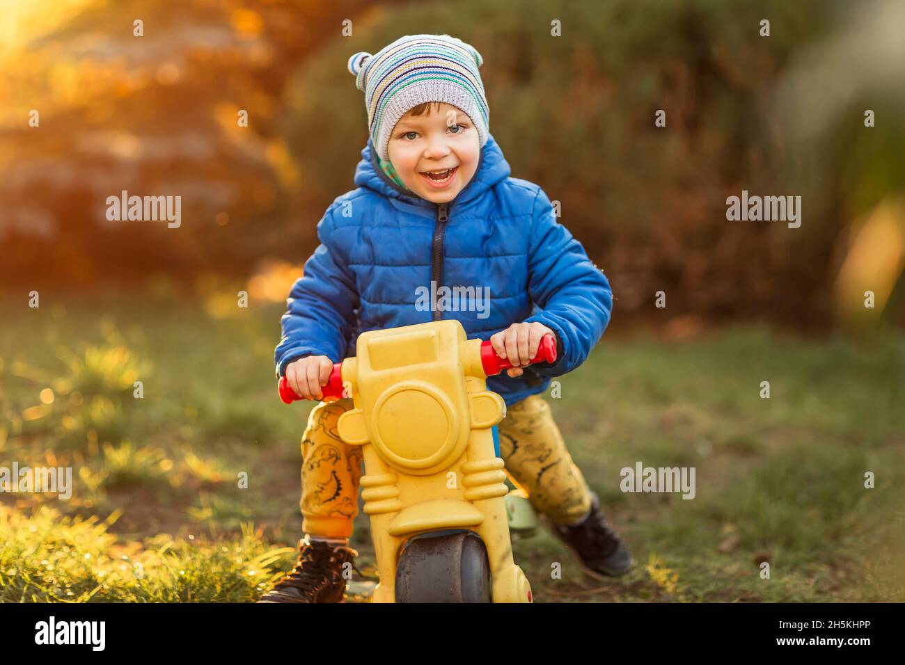 Ragazzino con occhi blu e giubbotto blu su giocattolo di plastica Foto Stock