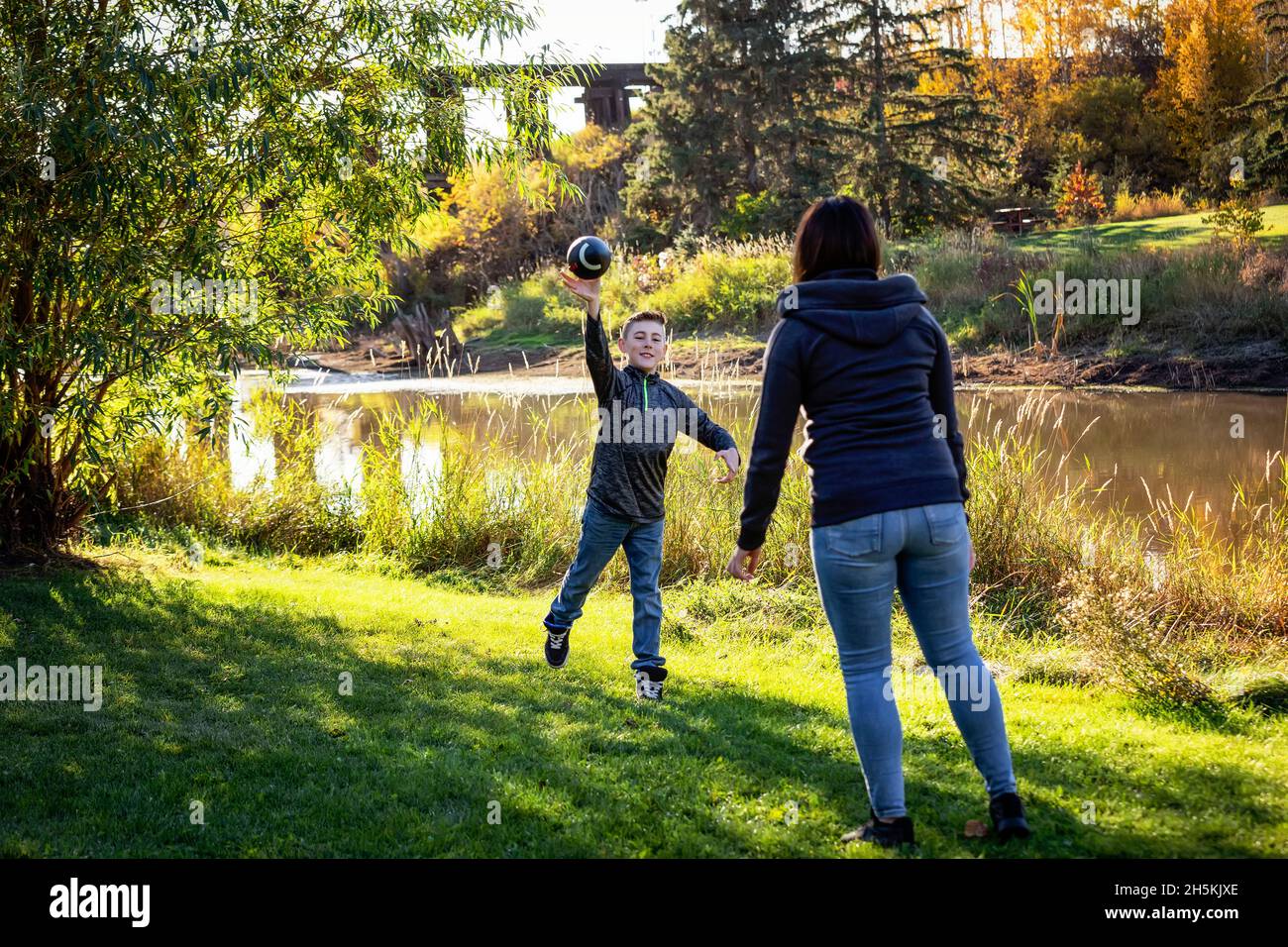 Madre che lancia un calcio con suo figlio in una bella giornata autunnale in un parco cittadino; St. Alberta, Alberta, Canada Foto Stock