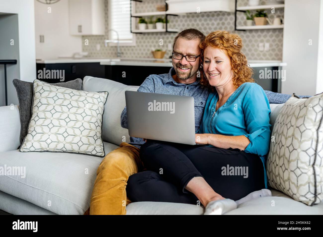 Coppia sposata seduta su un divano a casa utilizzando il loro computer portatile; Edmonton, Alberta, Canada Foto Stock