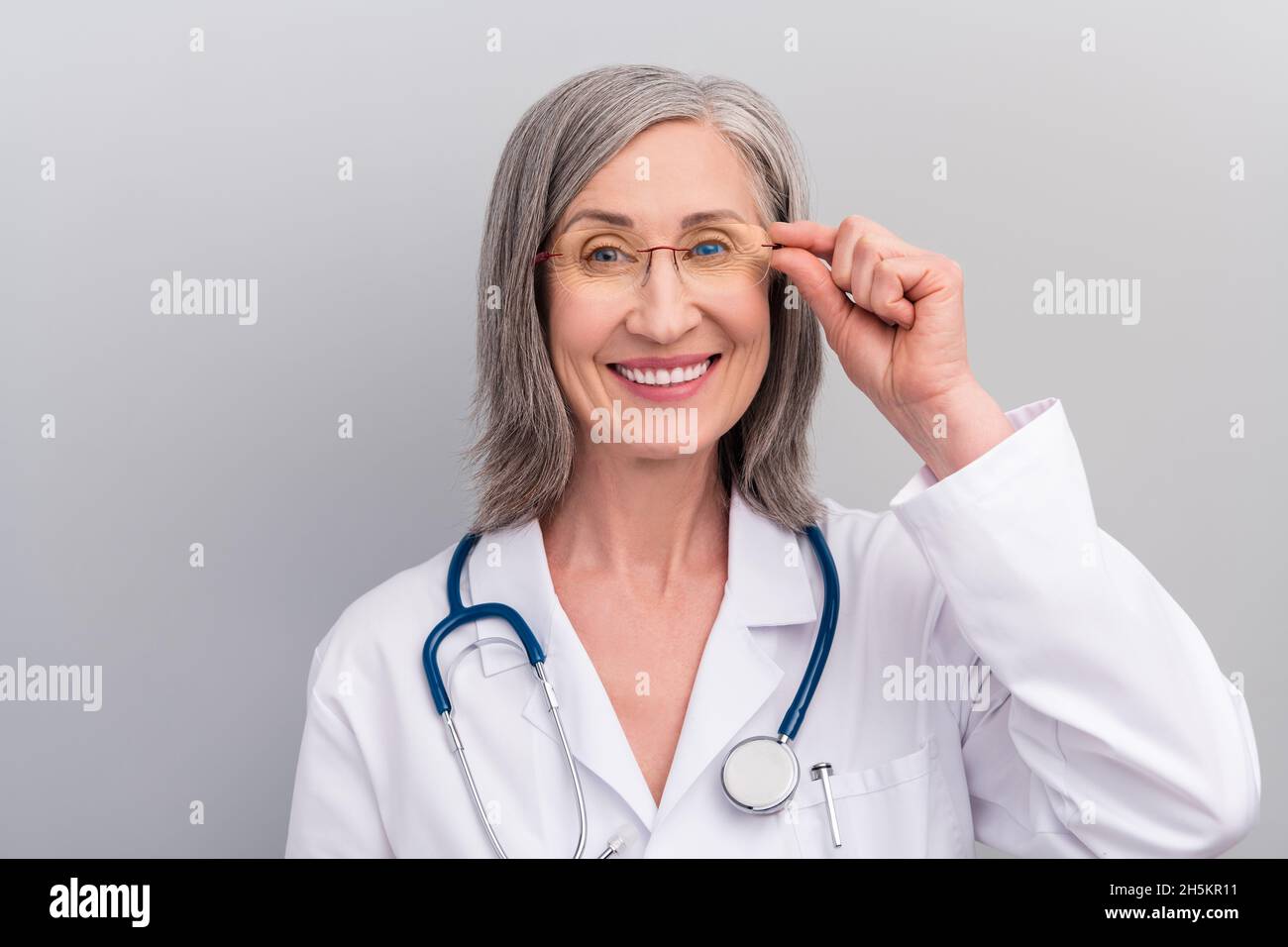 Foto di sicura positiva donna anziana doc vestito bianco uniforme braccio occhiali sorridente isolato grigio sfondo di colore Foto Stock