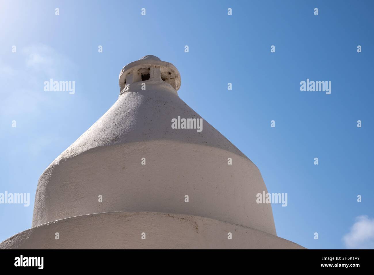 Camino rotondo imbiancato sulla parte superiore del tetto dell'edificio, isola greca, Grecia. Cerchio fumkestack costruzione esterna su un tetto casa. Backgrou cielo blu Foto Stock