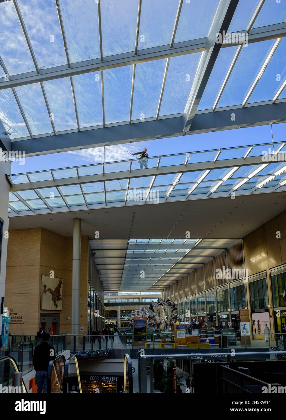 Un uomo che cammina su un tetto di vetro di un centro commerciale, pulendo il vetro. Foto Stock