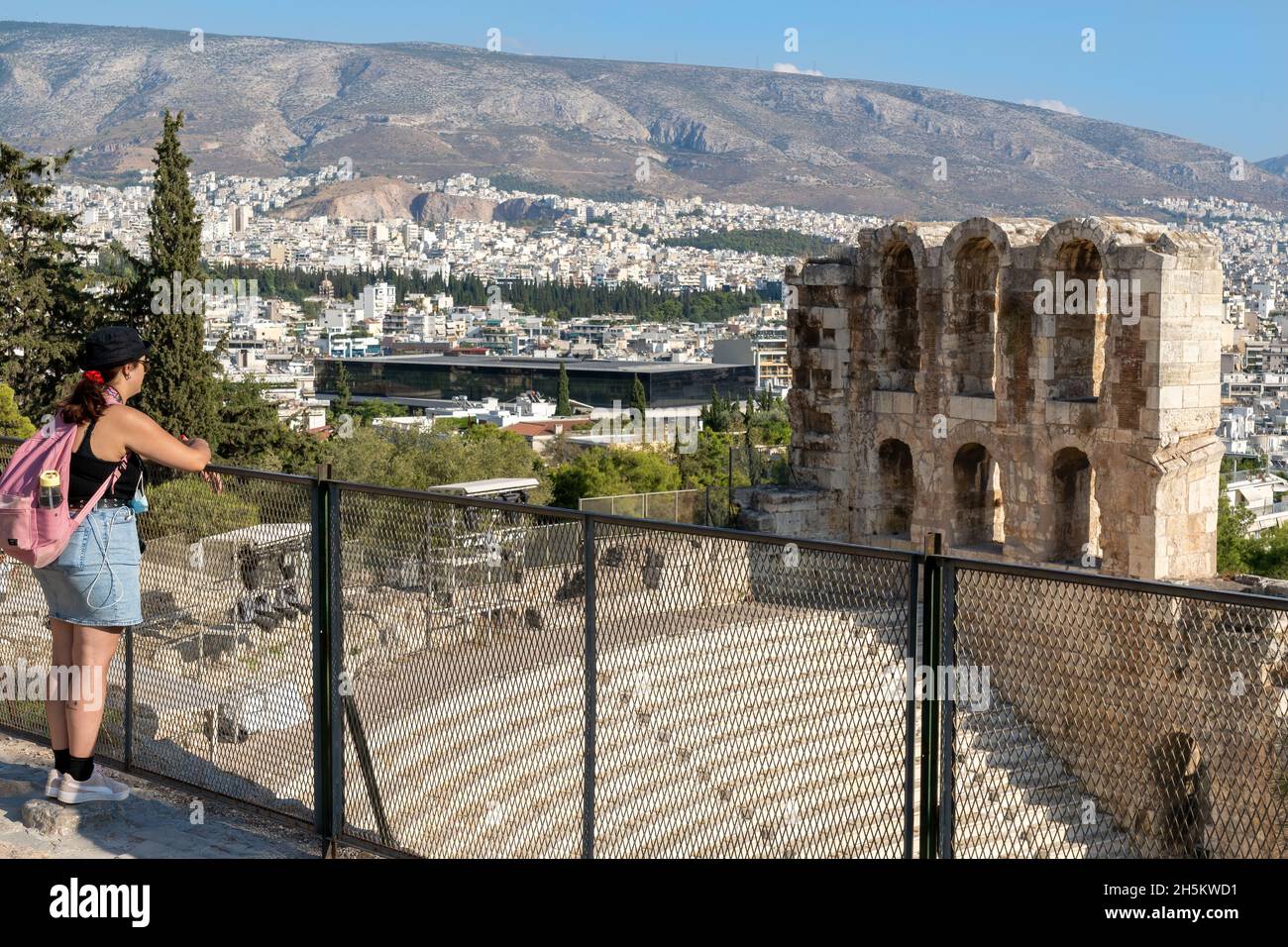 La giovane donna ammirerà la vista sull'Odeon di Erode Attico (o Erodion), l'antico teatro greco, il Museo dell'Acropoli e la città di Atene Foto Stock