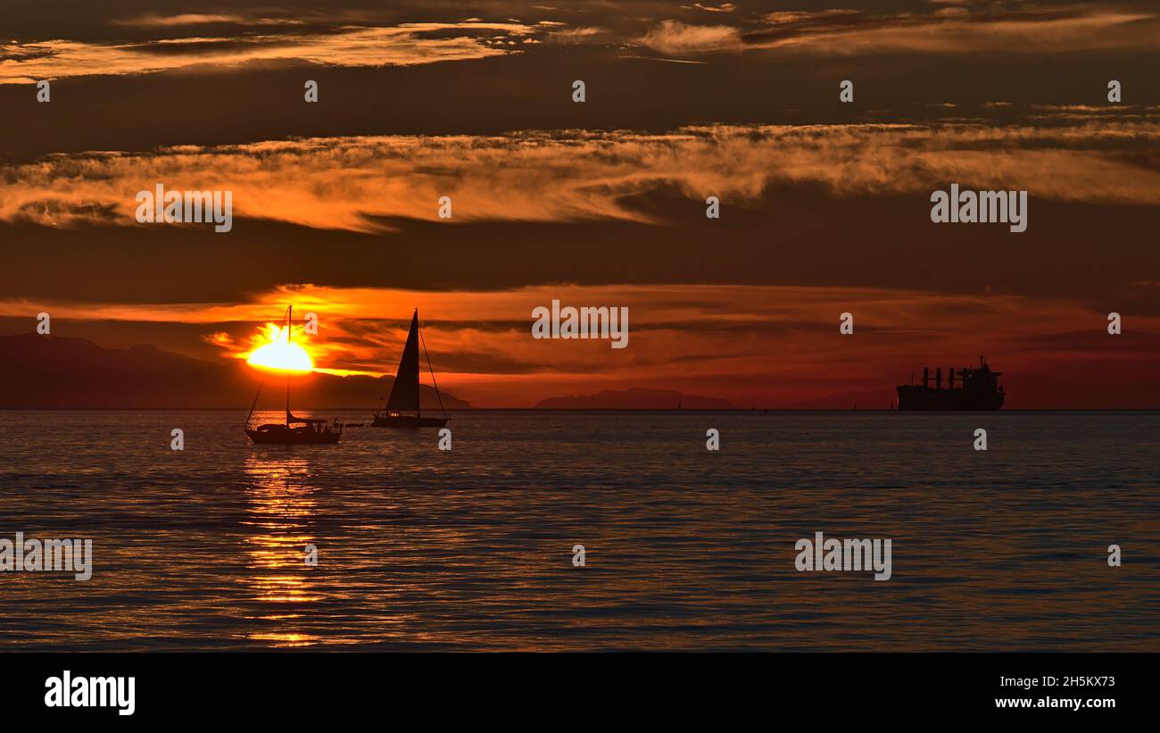 Tramonto su English Bay sulla costa di Vancouver, British Columbia, Canada, con la sera il sole che sparisce dietro le montagne di Vancouver Island. Foto Stock