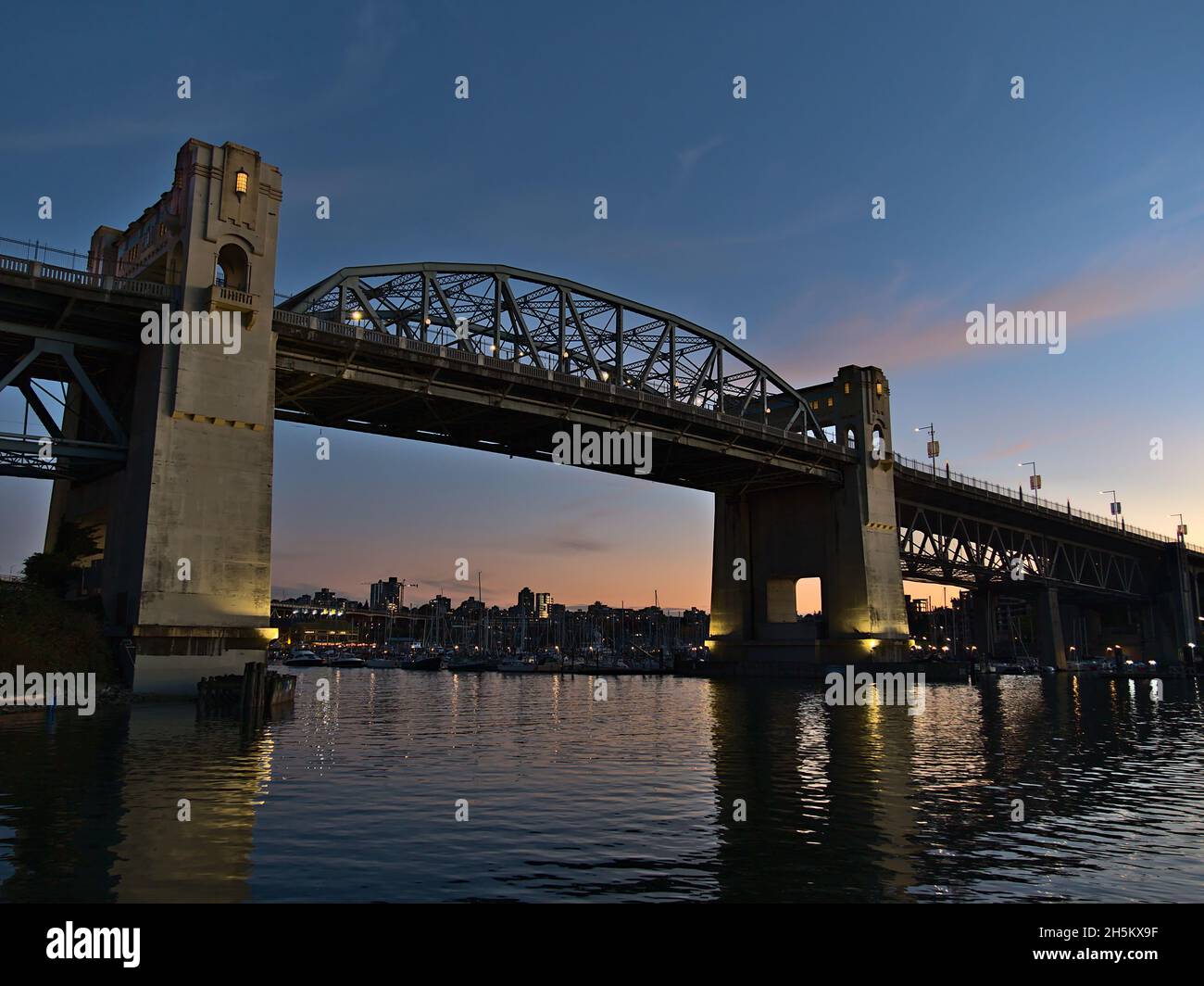 Ponte di Burrard Street alla luce della sera dopo il tramonto con colonne illuminate riflesse nell'acqua della baia di False Creek a Vancouver, BC, Canada. Foto Stock