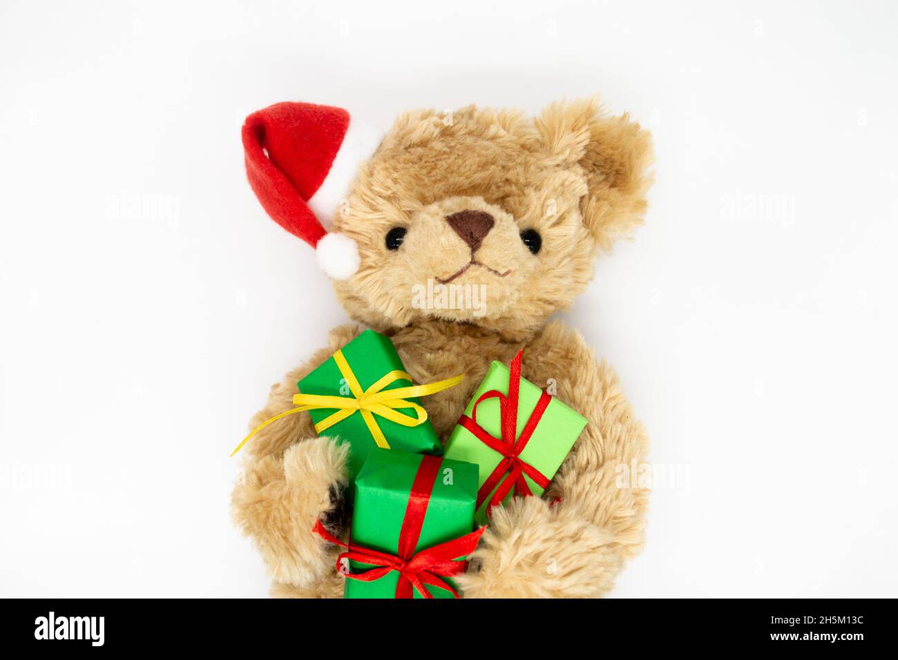 Un orsacchiotto peluche giocattolo in un cappello rosso di Babbo Natale con un pompom su un orecchio, tenendo le scatole regalo verdi nelle sue zampe. Sfondo bianco, spazio di copia. Il co Foto Stock