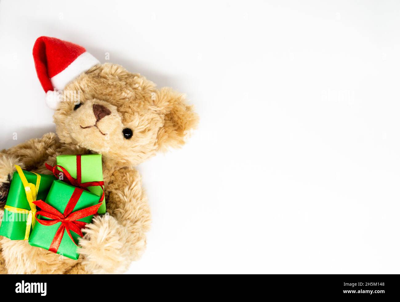 Un orsacchiotto peluche giocattolo in un cappello rosso di Babbo Natale con un pompom su un orecchio, tenendo le scatole regalo verdi nelle sue zampe. Sfondo bianco, spazio di copia. Il co Foto Stock