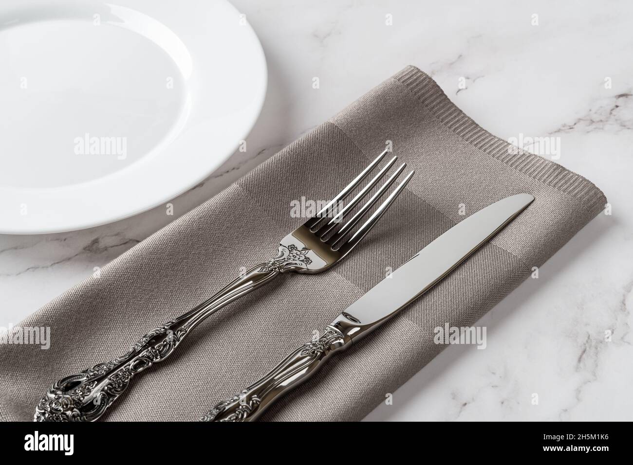 Elegante forchetta vintage e coltello da tavolo su un tovagliolo grigio per cena e un piatto bianco in porcellana sul tavolo in marmo. Stoviglie e posate per tavolo set. Vuoto Foto Stock