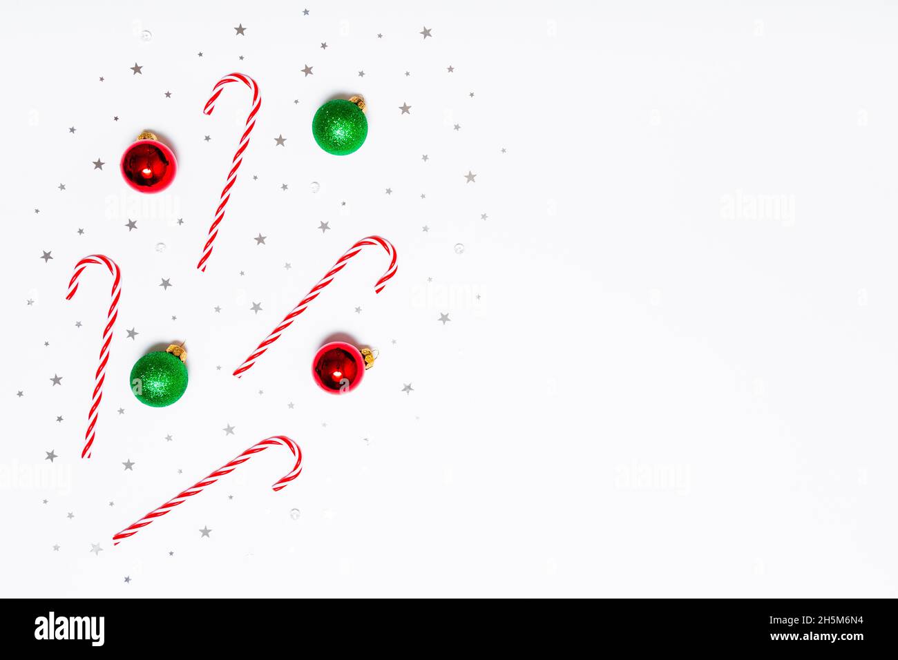 Piatto di Natale. Caramelle natalizie, palline rosse e verdi, stelle con glitter argento su sfondo bianco. Design piatto, vista dall'alto, spazio di copia Foto Stock