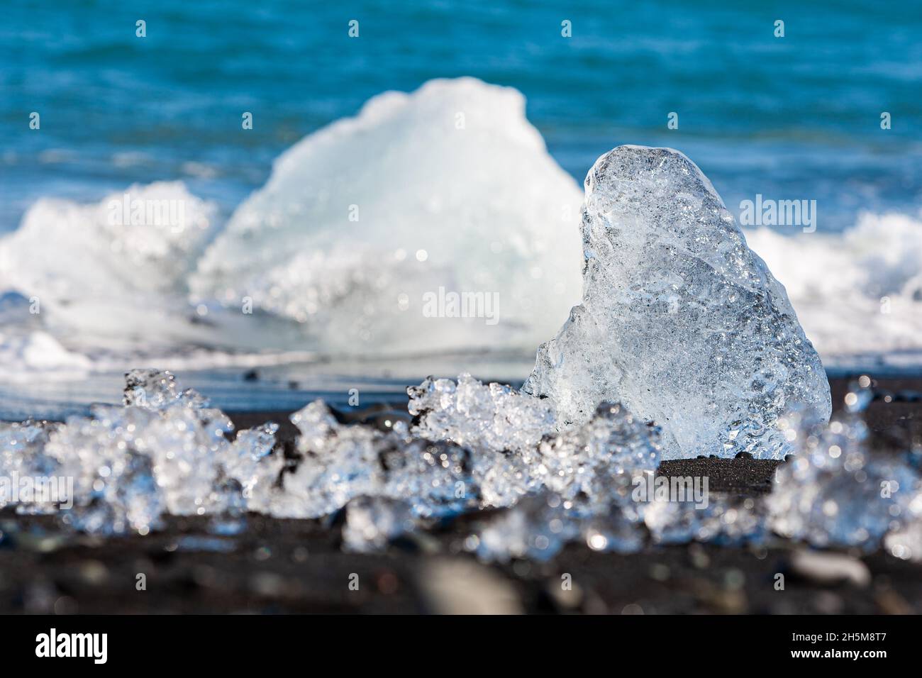 Cambiamento climatico concetto di riscaldamento globale, primo piano di ghiaccio fondersi su una spiaggia vulcanica di sabbia nera in Islanda, un iceberg nelle onde può essere visto nel b Foto Stock
