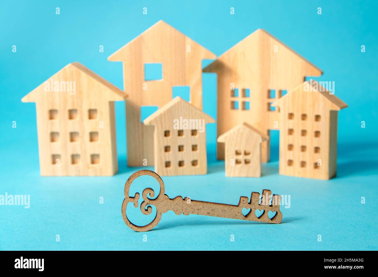 Chiave sullo sfondo di case in legno in miniatura. Concetto di acquisto e vendita di immobili. Alloggi a prezzi accessibili. Ipoteche e prestiti. Affittare un appartamento. Foto Stock