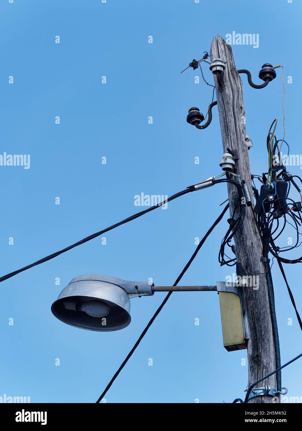 Scatto verticale di una luce stradale fissata a un vecchio palo di legno contro un cielo blu durante il giorno Foto Stock