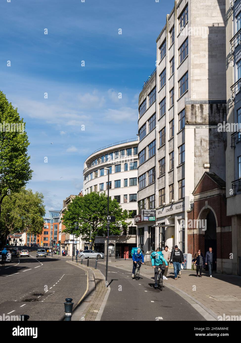 I ciclisti e i pedoni passano accanto agli uffici illuminati dal sole in Baldwin Street, nel centro di Bristol. Foto Stock