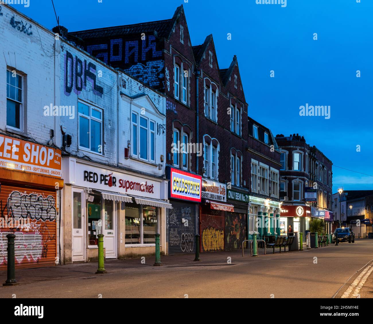 I negozi sono navati di notte lungo East Street a Bedminster, Bristol. Foto Stock