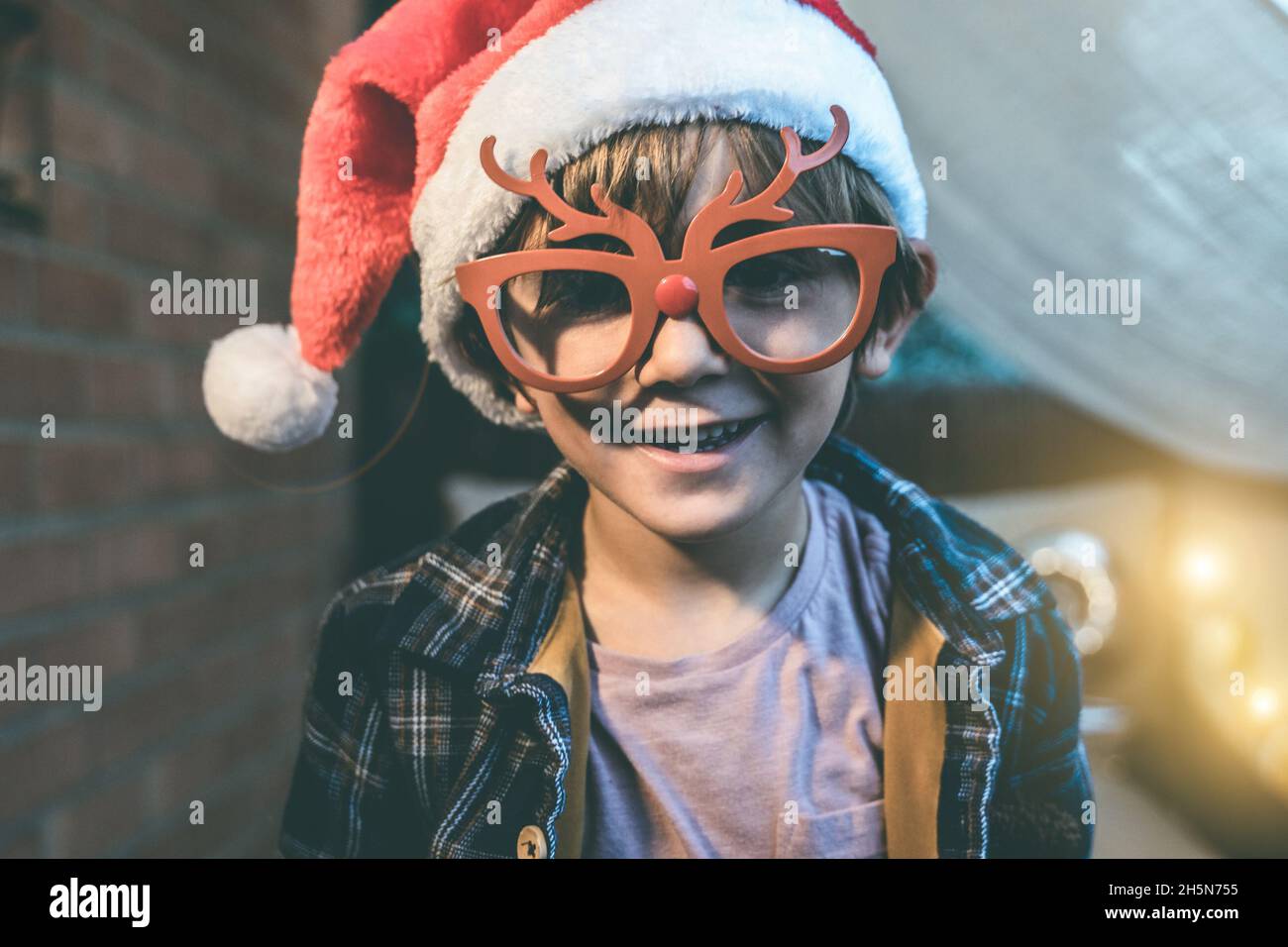 Ragazzo giovane che si diverte indossando il cappello di Babbo Natale e i bicchieri di Rudolf di Natale - Focus on Face Foto Stock