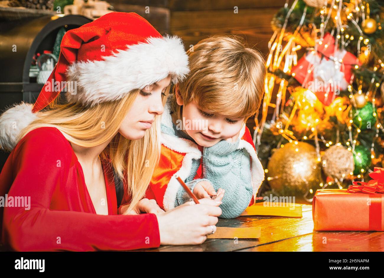 Giovane madre e figlio scrivono una lettera a Santa. Vacanze invernali e concetto di infanzia. Assistente di Santa con wishlist per Santa. Foto Stock