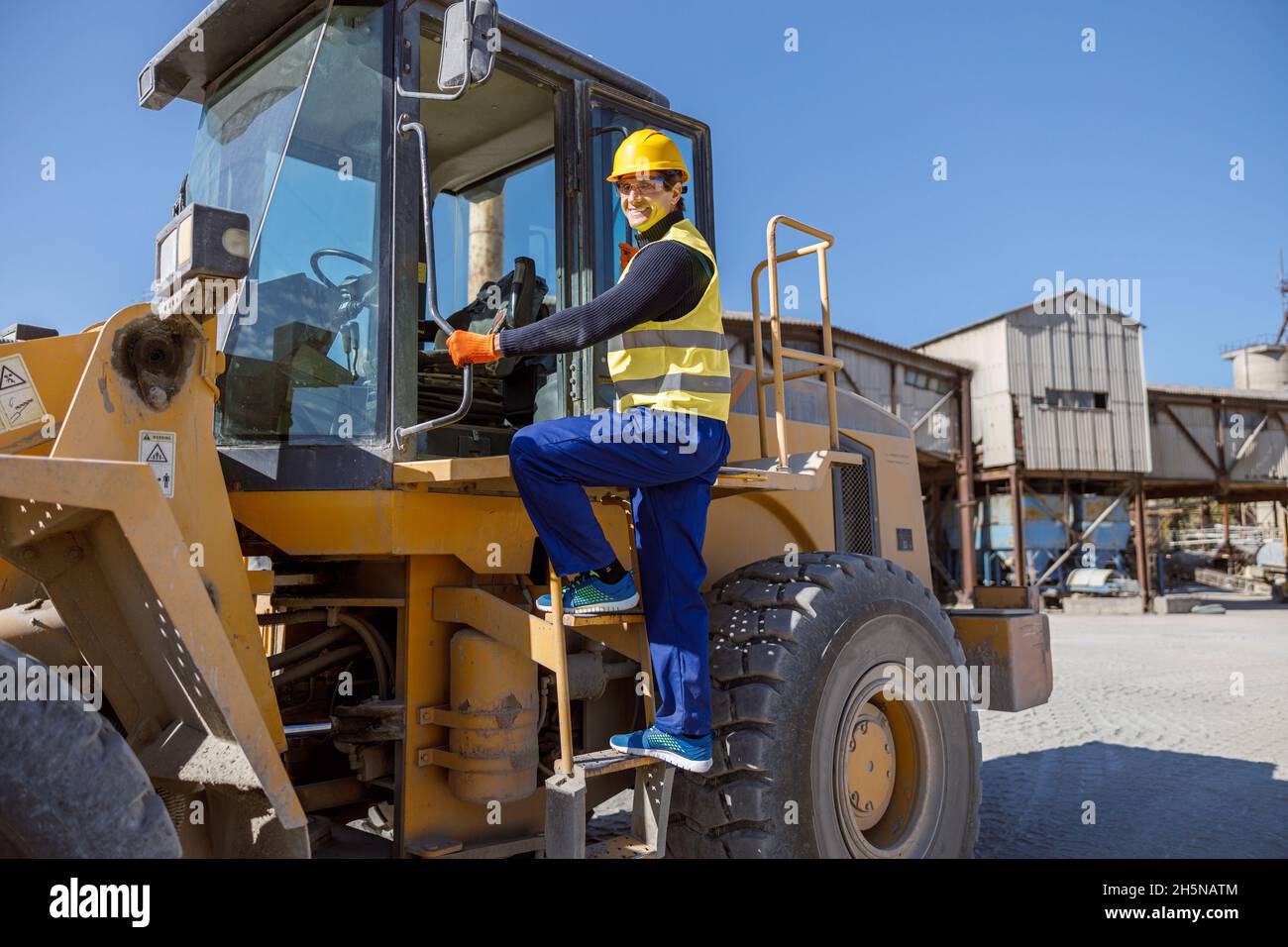 Allegro ingegnere maschile in piedi sulle scale del trattore all'aperto Foto Stock