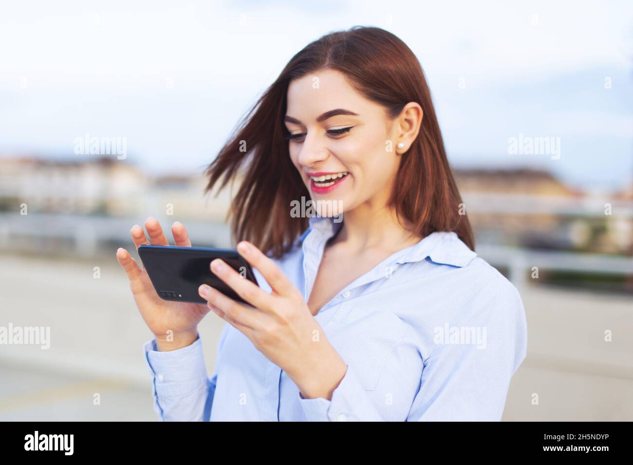 Giovane donna d'affari caucasica redhead messaggi su smartphone e ridere all'aperto Foto Stock