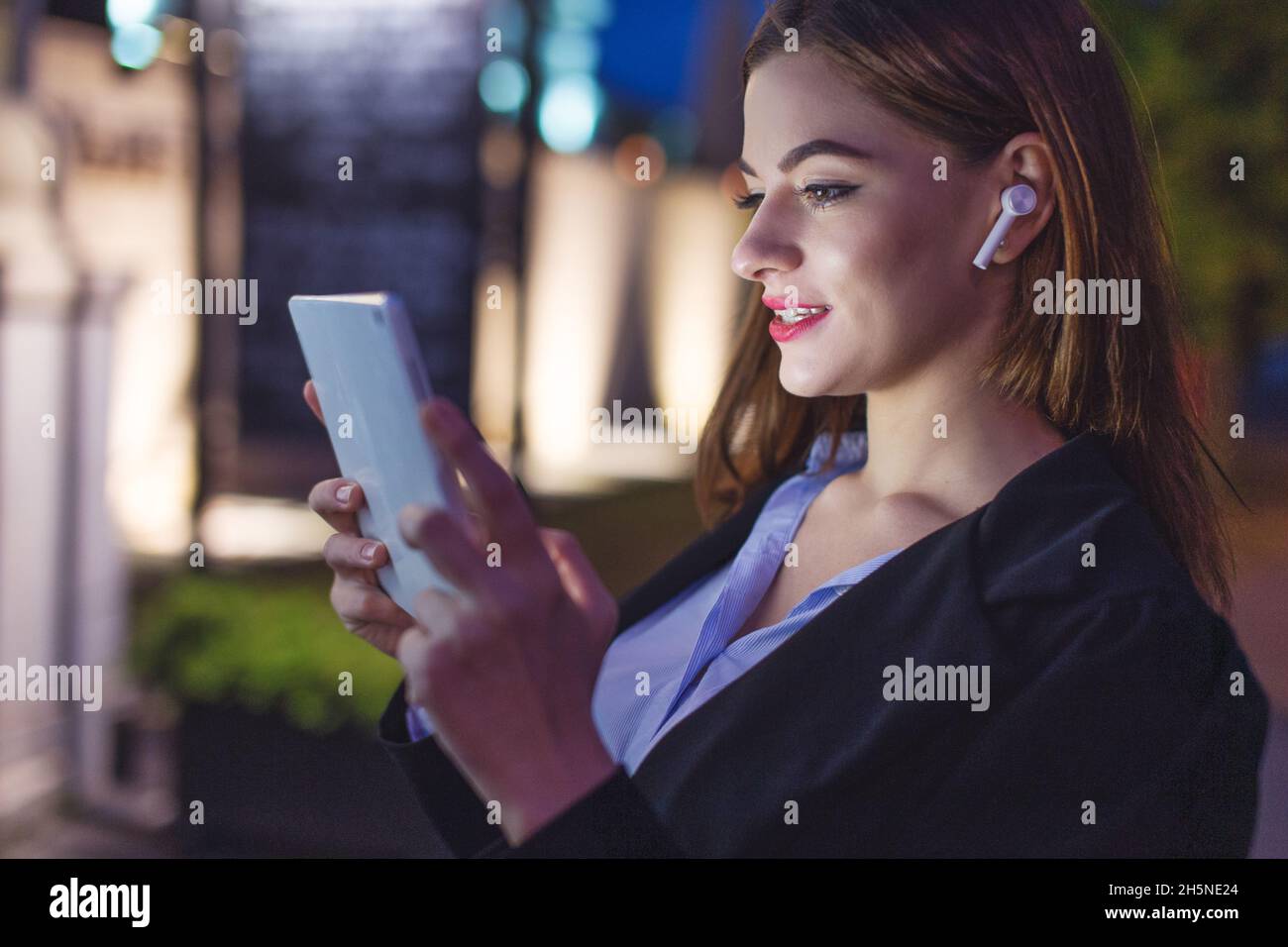 Giovane donna d'affari con dispositivo vivavoce che utilizza tablet di notte in città, assistenza clienti Foto Stock