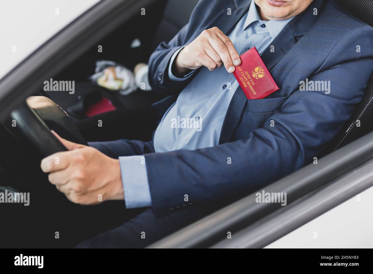 Concetto di immunità parlamentare. L'uomo in abito blu mostra una carta d'identità rossa o un pass. Un importante dipendente intoccabile del ministero sta guidando un'automobile. duma di stato Foto Stock