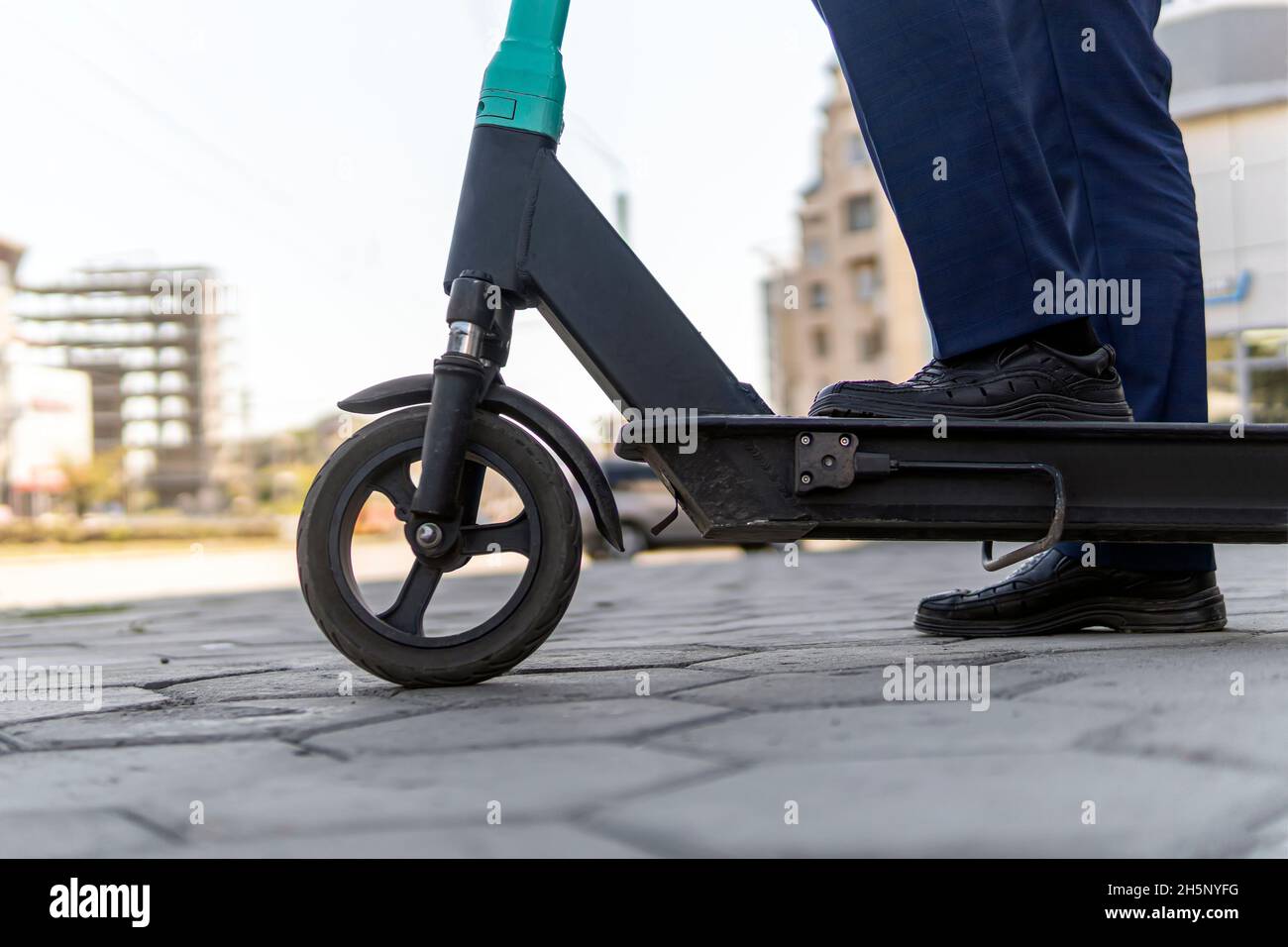 Primo piano di gambe uomo in tuta a guida scooter elettrico in città. Uomo d'affari sconosciuto in abito classico giro su scooter elettrico mobile. Moderno ed ecologico Foto Stock