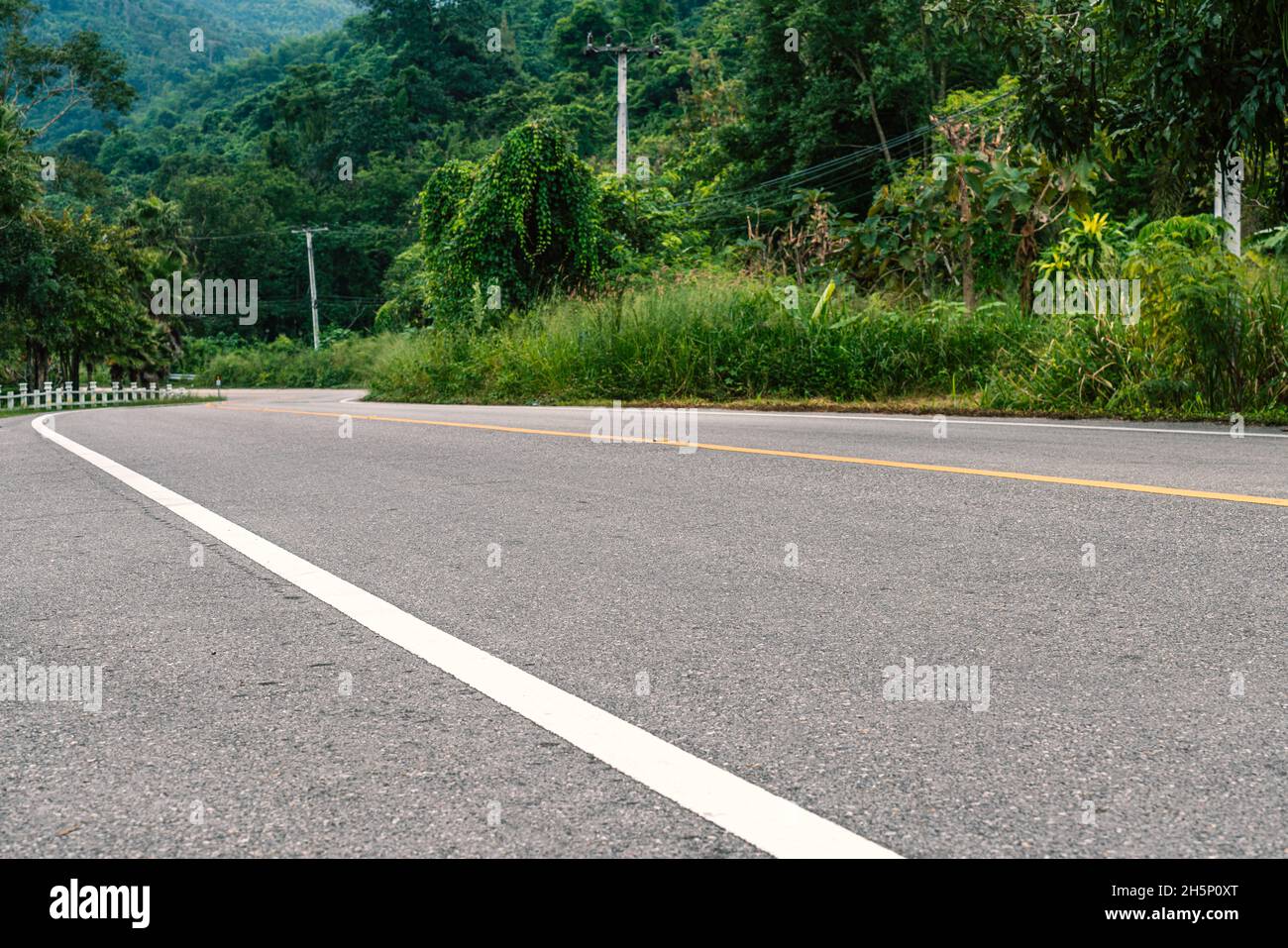 Strada a due corsie nel paese della Thailandia, vecchio stile polo di elettricità lungo la strada, vista prospettica della foresta di montagna, basso angolo di vista. Nessun veicolo Foto Stock