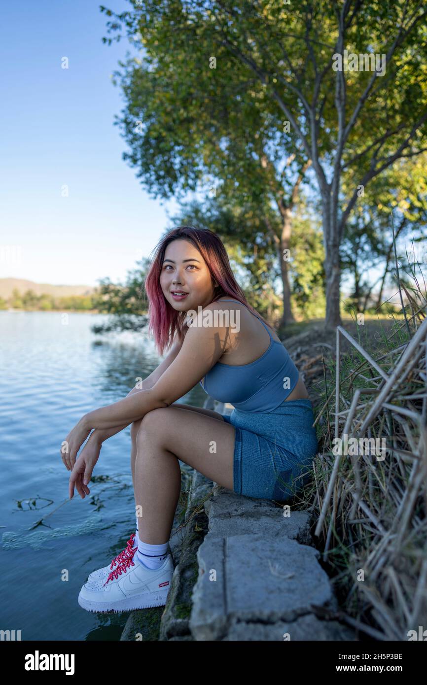 Giovane donna asiatica in luce del sole appled seduta sulla riva di un lago idilliaco Foto Stock