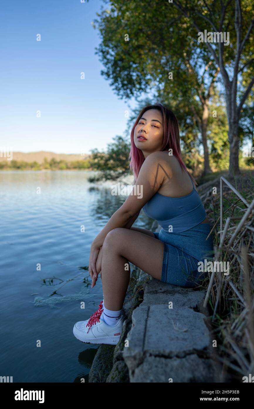 Giovane donna asiatica in luce del sole appled seduta sulla riva di un lago idilliaco Foto Stock