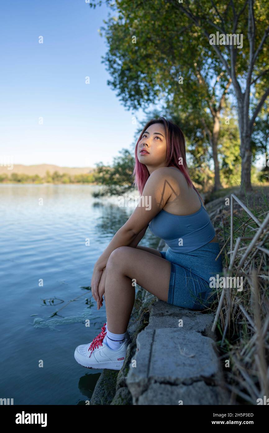 Giovane donna asiatica in luce del sole appled seduta sulla riva di un lago idilliaco Foto Stock