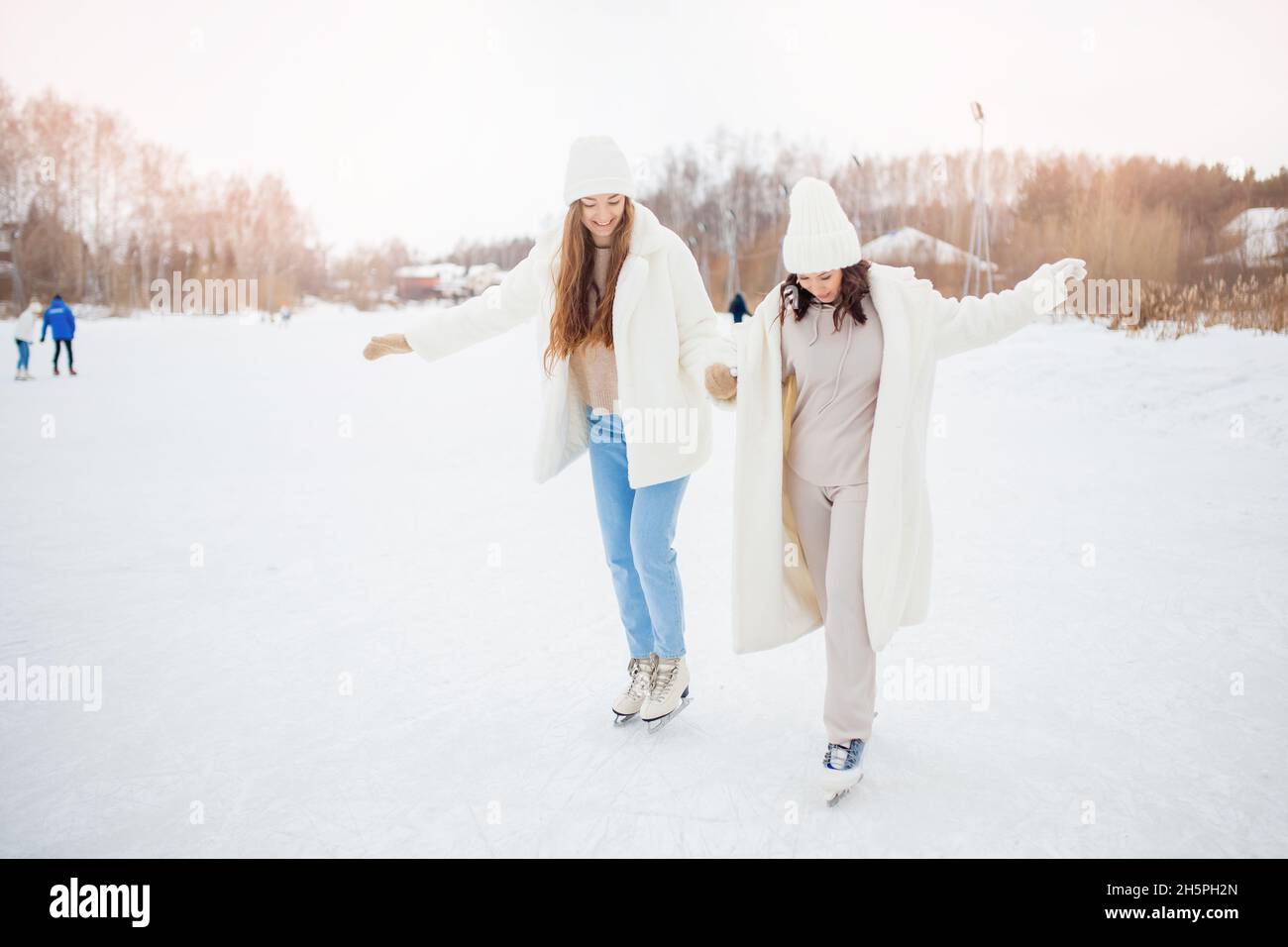 Gli amici delle donne imparano a pattinare sulla pista di pattinaggio in inverno. Aiuto concettuale, formazione, ricreazione sana, stile di vita. Foto Stock