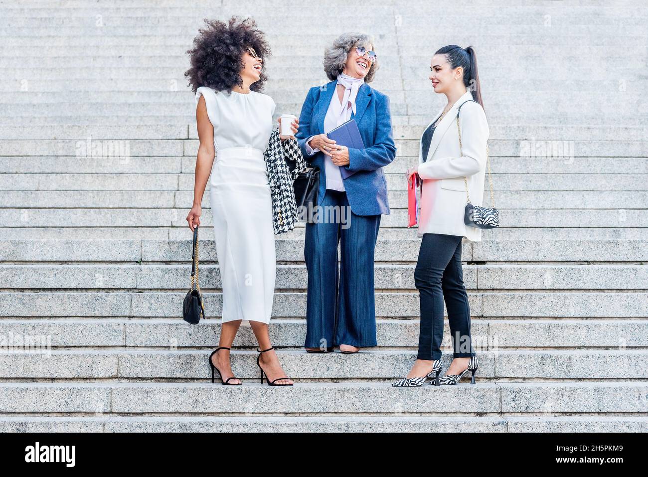tre donne d'affari ridono mentre si levano in piedi sulle scale Foto Stock