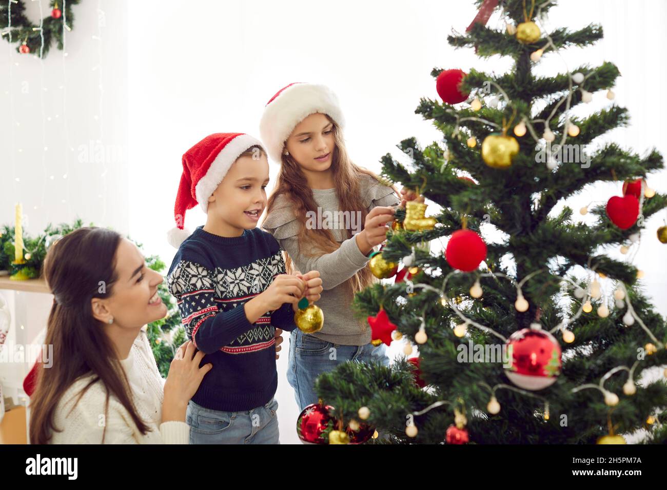 Madre felice e bambini piccoli appendere ornamenti sul loro albero di Natale insieme Foto Stock