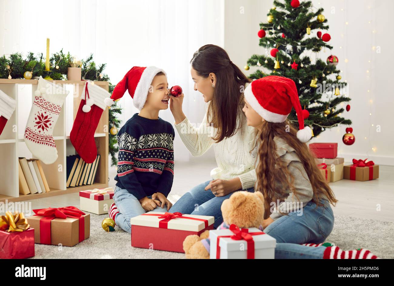 Felice madre e bambini divertirsi con gli ornamenti natalizi a casa il giorno di Natale Foto Stock