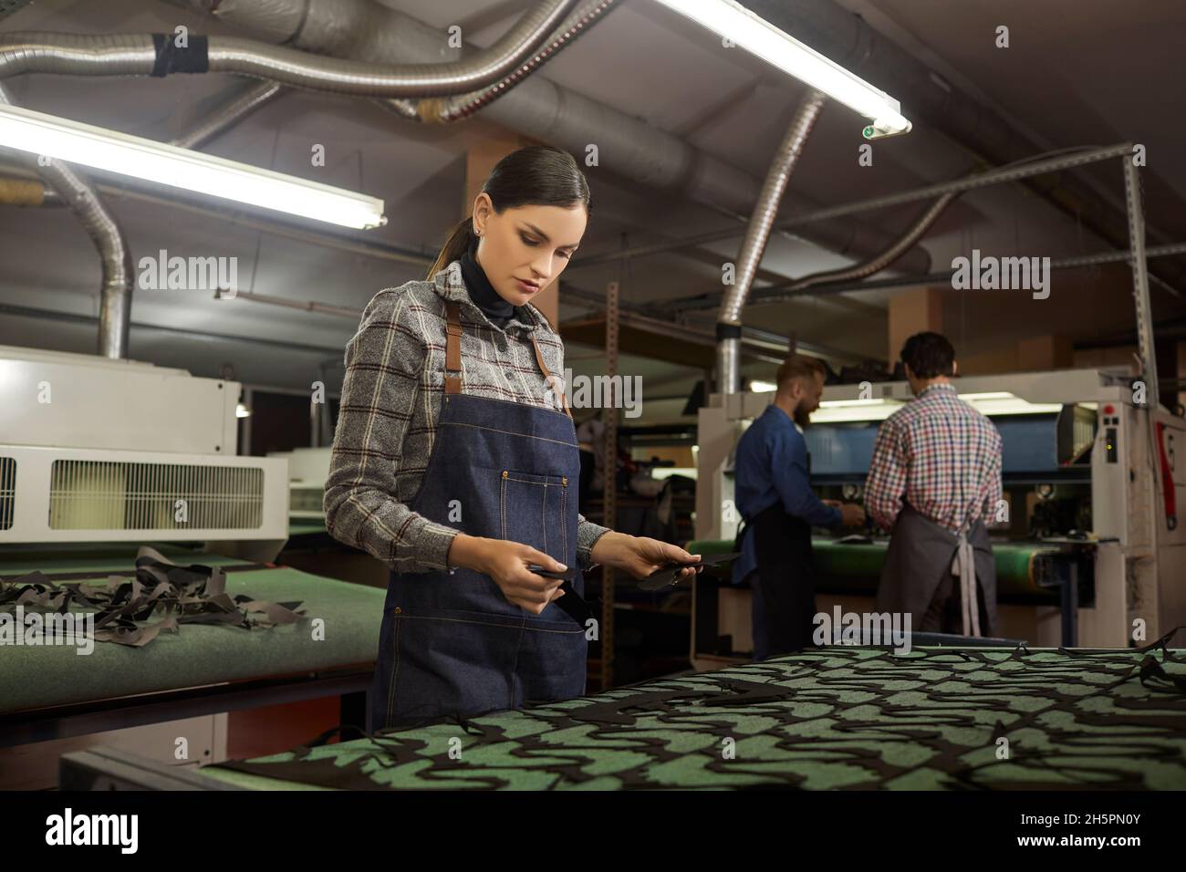 Lavoratrice femminile che lavora con la macchina da taglio in officina della fabbrica di calzature Foto Stock