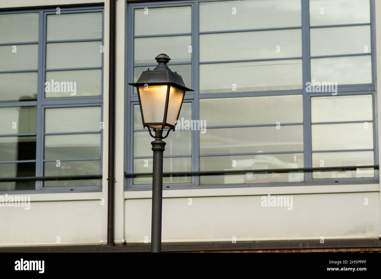 lampione illuminato, sullo sfondo delle finestre di un edificio moderno, nella città metropolitana. Foto Stock