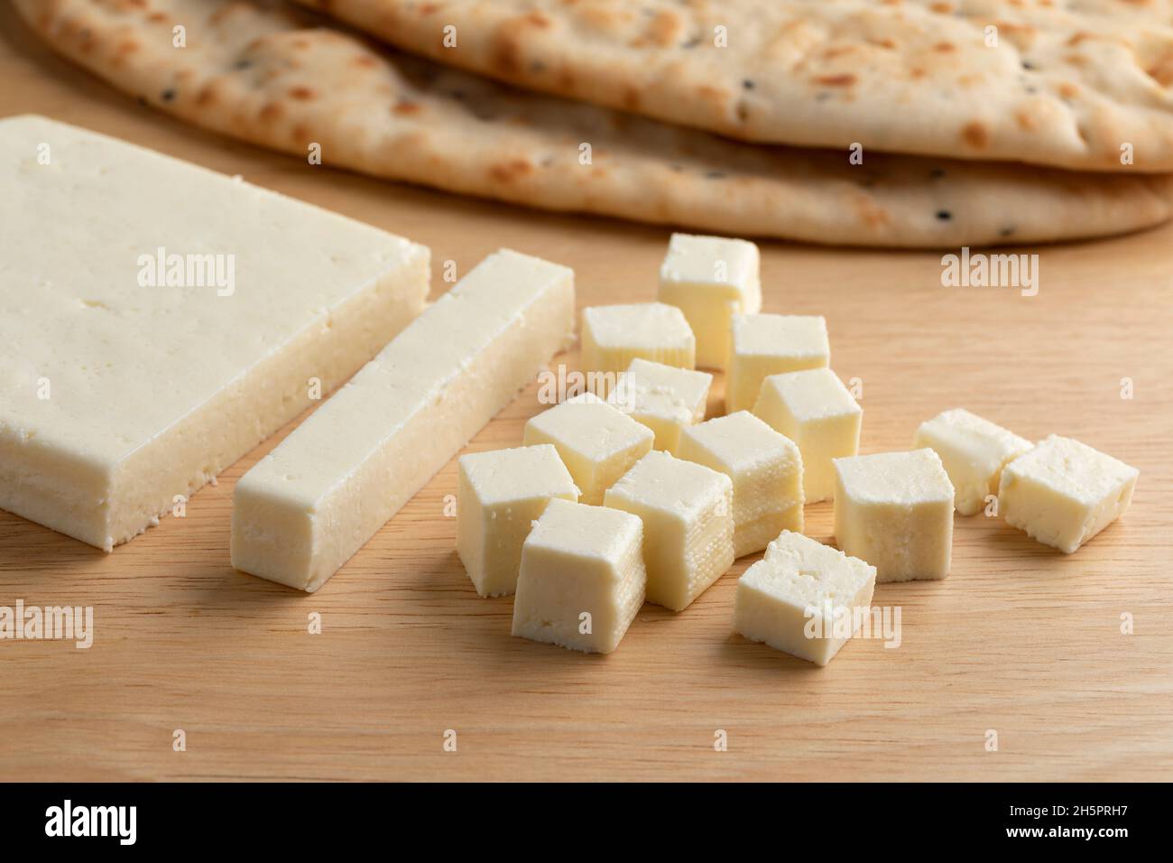 Fetta di formaggio paneer indiano, cubetti e naan sullo sfondo Foto Stock