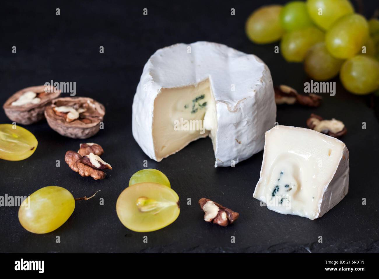 Tipo di formaggio Brie. Formaggio morbido con uva e noci su sfondo nero Foto Stock
