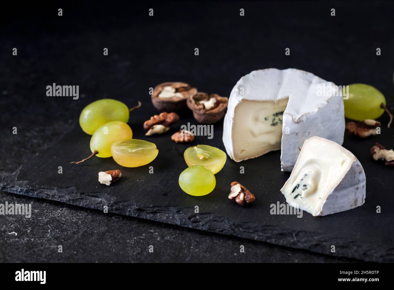 Tipo di formaggio Brie. Formaggio morbido con uva e noci su sfondo nero Foto Stock